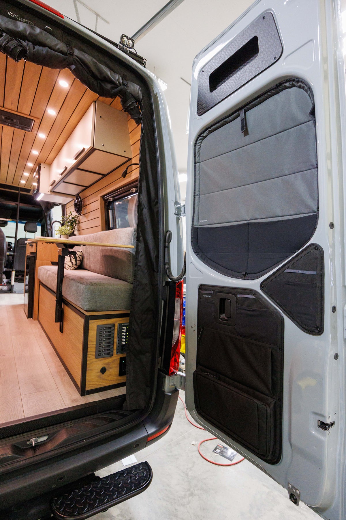 Open rear doors of a Mercedes Sprinter camper van with black hexply storage cubbies installed at the top of both cargo doors.